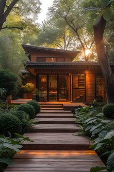 a wooden walkway leading to a house surrounded by trees and bushes with the sun shining on it