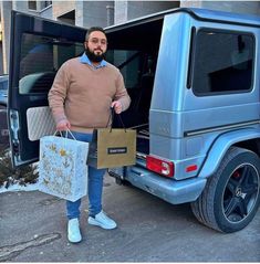 a man holding shopping bags standing in front of a car