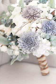 a bridal bouquet with blue and white flowers on the back of a chair in front of a window