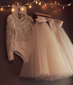 two dresses hanging up on a wall with lights in the background and an image of a dress