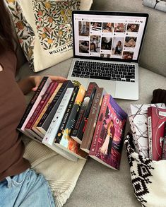 a woman is sitting on the couch with books in front of her lap top computer