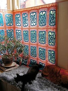 two cats sleeping on a couch next to a potted plant in front of a window