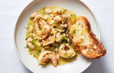 a white plate topped with pasta and shrimp next to a piece of toasted bread