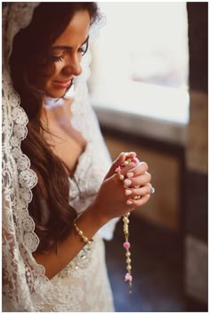 a woman wearing a veil and holding a rosary in her right hand while standing next to a window