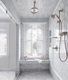 a bathroom with white marble walls and floor, along with a large window that has shutters in it