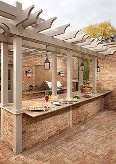 an outdoor kitchen with brick flooring and pergolated roof over the counter area