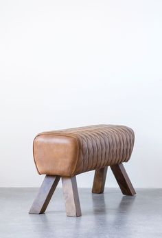 a brown leather bench sitting on top of a cement floor next to a white wall