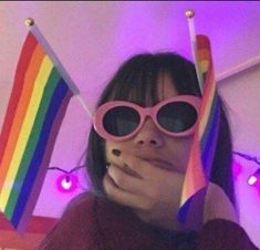 a woman wearing pink sunglasses and holding up two rainbow colored sticks in front of her face