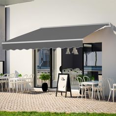 an outdoor dining area with white chairs and tables under a gray awning over it