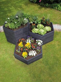 three planters with different types of flowers in them on the grass next to a garden path