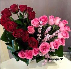 a vase filled with pink and red roses on top of a white table next to a plant