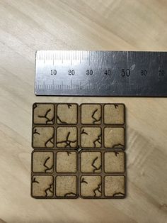 a ruler is next to two square shaped coasters with birds on them, and one has four smaller squares in the middle