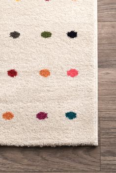 a white rug with multicolored dots on the floor in front of a wooden floor