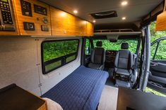 the interior of an rv with wood paneling and blue bedding, windows on both sides