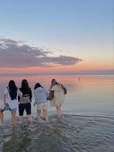 four girls are standing in the water watching the sun go down over the ocean at sunset