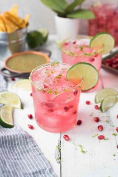 two glasses filled with pink lemonade, lime and pomegranate garnish