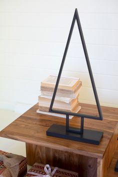 a stack of books on top of a wooden table next to a metal triangle sculpture