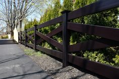 a wooden fence is shown in front of some trees and bushes on the side of a road