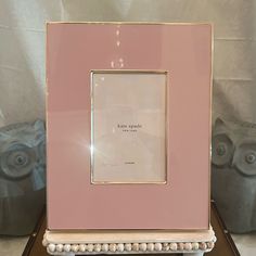 a pink and gold frame sitting on top of a wooden table next to an owl statue