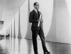 a man in a suit and tie standing on a wooden floor next to tall pillars