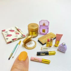 a person's finger next to various cosmetics and other items on a white surface