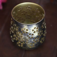 a metal cup sitting on top of a wooden table next to a pink flower vase