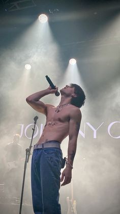 a man with no shirt on singing into a microphone in front of some spotlights