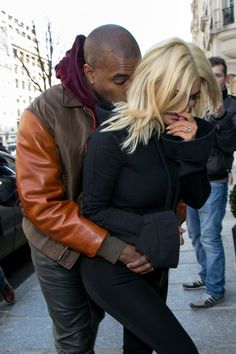 a man and woman standing next to each other on a sidewalk with cars behind them