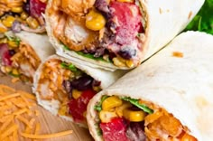 three burritos on a cutting board with shredded cheese and other ingredients in the background