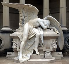 an angel statue sitting on top of a stone bench in front of a tall building