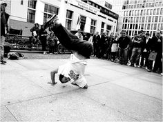 a man doing a handstand on the sidewalk in front of a group of people