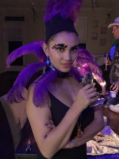 a woman with purple feathers on her head is holding a candle and looking at the camera