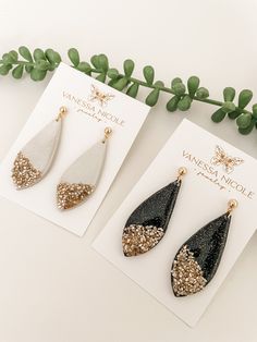 two pairs of black and white earrings with gold glitters on them next to a card