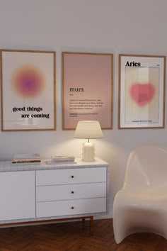 a white chair sitting next to a table with a lamp on it and two pictures above it