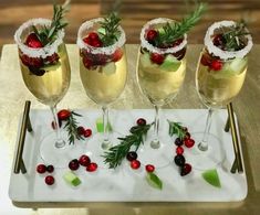 four glasses filled with wine and garnishes on a white tray next to greenery