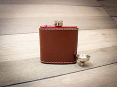 a brown leather flask with a silver cup next to it on a wooden floor