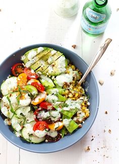 a blue bowl filled with cucumbers, tomatoes and other veggies next to a spoon