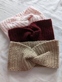 three crocheted headbands on top of a bed with one tied up