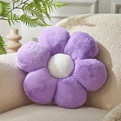 a purple flower shaped pillow sitting on top of a couch next to a potted plant