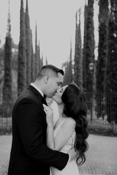 a bride and groom kissing in front of some tall trees at their wedding reception venue