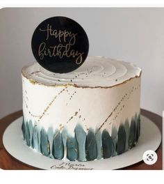 a white and blue cake with a happy birthday sign on top, sitting on a wooden table