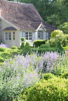 a house surrounded by lush green bushes and purple flowers