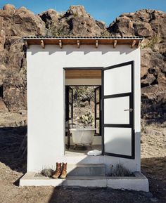 a small white building with a tub in the doorway and some rocks on the other side