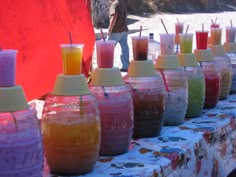 there are many vases with different colored drinks on the table next to each other