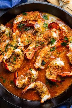 a pan filled with shrimp and sauce on top of a blue towel next to bread