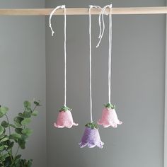 three crocheted bell ornaments hanging from a clothes line next to a potted plant