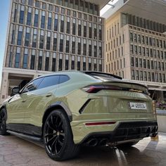 the rear end of a green sports car parked in front of a building with large windows