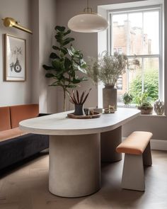 a dining room table and bench with potted plants in the window sill next to it