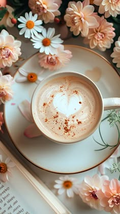 a cup of cappuccino on a saucer surrounded by flowers and an open book