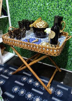 a wicker tray with wine bottles and glasses on it in front of a green wall